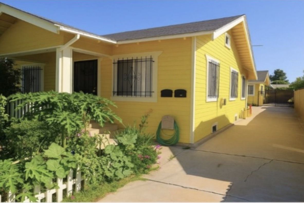 Yellow two-unit duplex with a shared front walkway and mature landscaping in Southern California